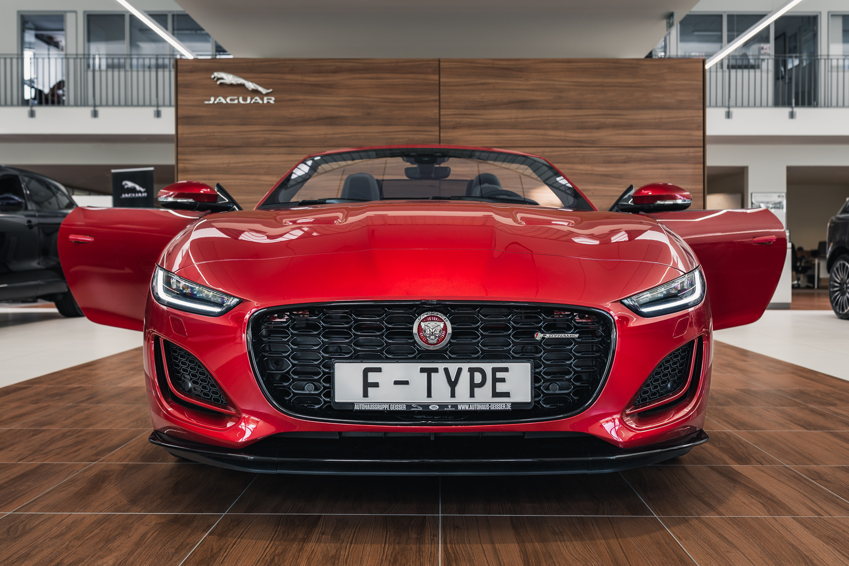 Das Sportwagenmodell F-Type von Jaguar in der Cabrio-Variante wurde hier frontal vor der Holzoptikwand im Showroom des Autohauses fotografiert. Im Fokus stehen ganz klar der sportliche Look und das Scheinwerfer-Design des Autos. Die Lackfarbe ist Firenze Red.
