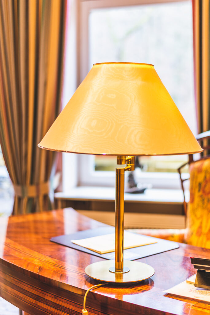 Klassisches Interieur im Hotel – Lampe mit goldenem Sockel und Holzschreibtisch
